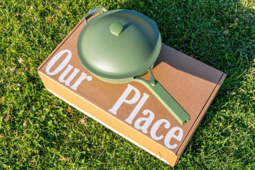 A custom cardboard box from Our Place with their logo on it, and a green pan sitting on top of it