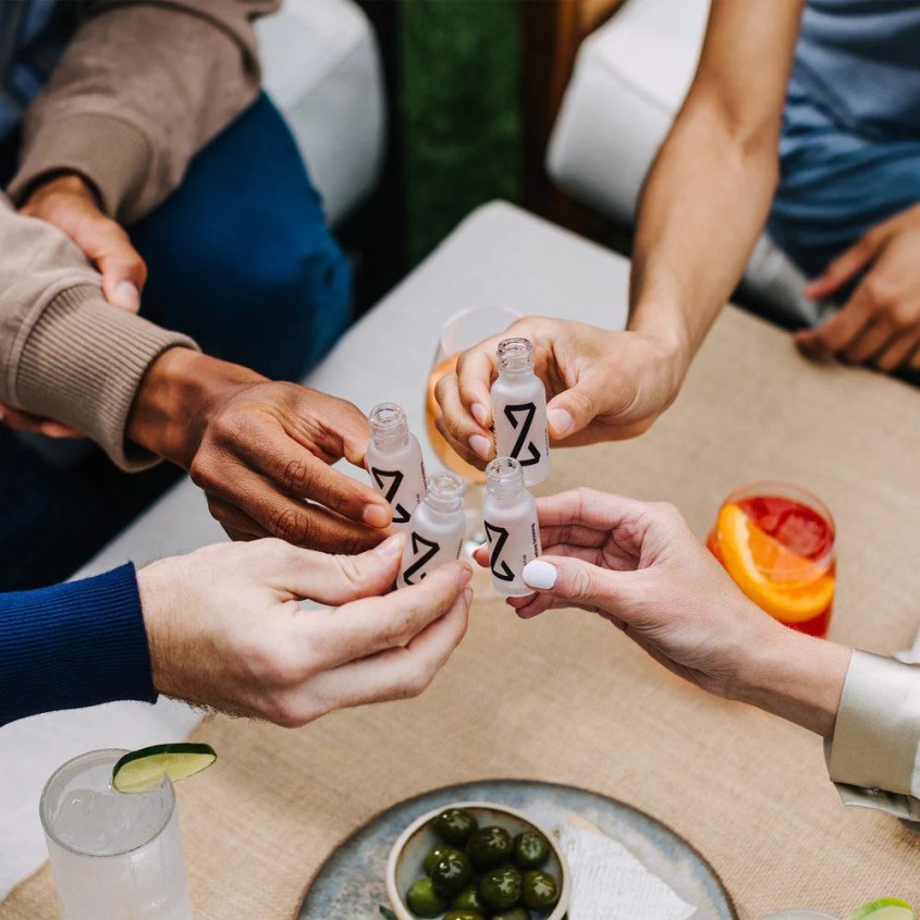 A close-up of people's hands holding Zbiotics' probiotic drinks in the act of a cheers