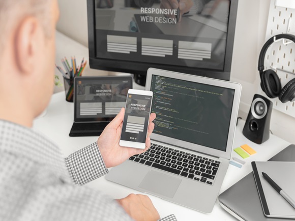 Businessman/web programmer testing responsiveness at work with a smartphone, showing the website on the screen. All screen graphics are made up id1306731001