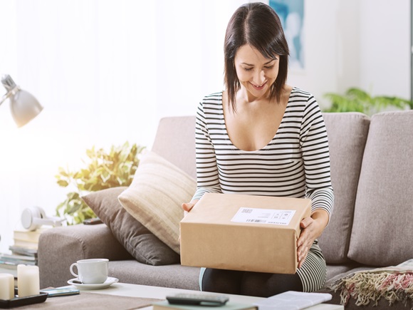 Smiling young woman at home on the couch, she has received a postal parcel, online shopping and delivery concept _id1056735011