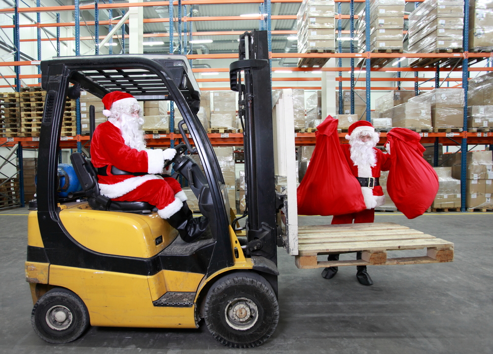 Two santa clauses as a workers in modern storehouse full of goods. One on forklift, another is lifting sacks full of presents._id86617489
