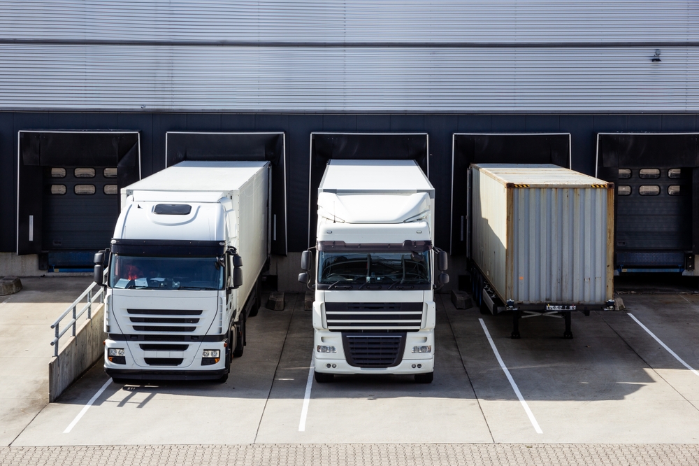 Trucks and trailers in front of a row of loading docks with shutter doors at an industrial warehouse._id2535123693