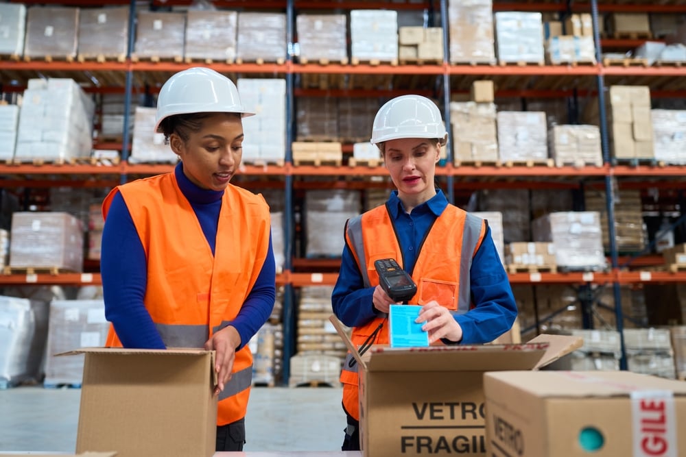 Two women scanning parcels and packing products into kits for shipping in a warehouse