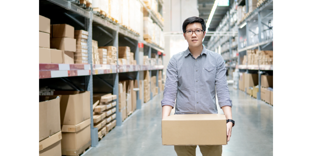 Young Asian man carrying cardboard box between row of shelves in warehouse. Shopping warehousing or working pick and packing concepts_id1284908767