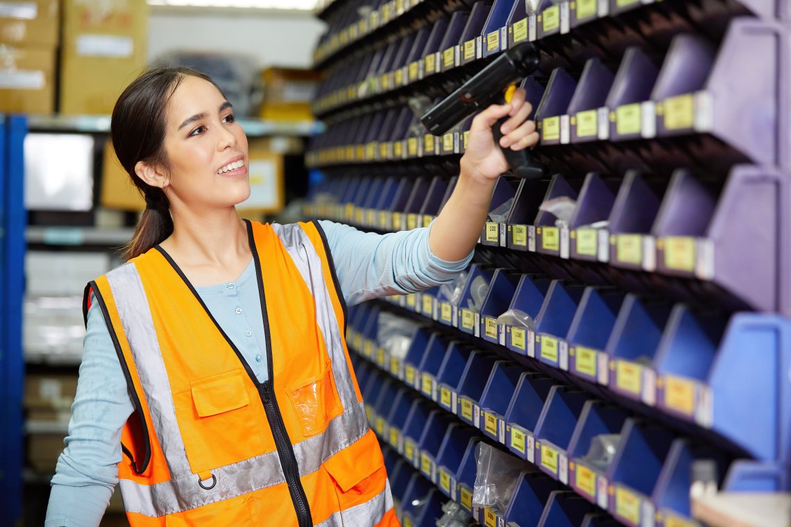 A worker in an orange safety vest holds a scanner up inventory storage bins.