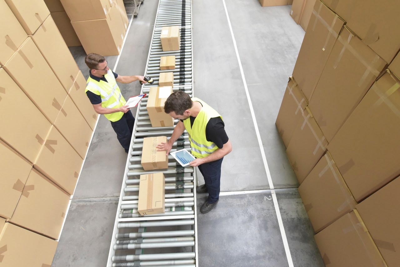 Photo of two warehouse associates in with boxes on a conveyor belt.