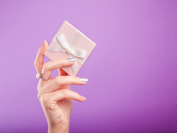 Female hands with beautiful manicure holding a small gift box on violet background_id768429292