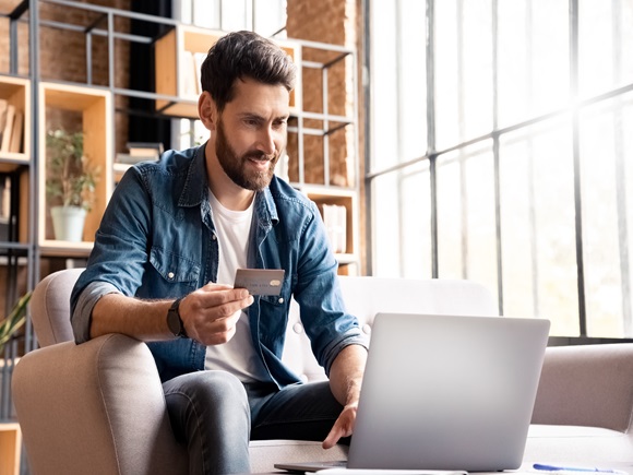 Happy smiling man buying, shopping or paying online with bank card and laptop. Male customer doing internet purchase using web banking service looking at computer screen making secure payment_id2376994801