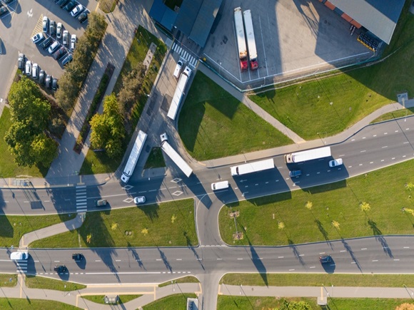 Aerial view of a busy road intersection with several trucks and cars. The image shows vehicles navigating through a complex road layout with green spaces and parking areas nearby_id2585538443