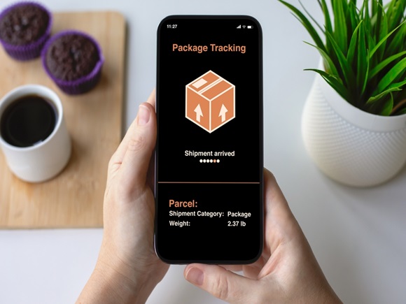 Woman hands holding phone with app tracking delivery package on screen background table with coffee and cakes in cafe_id2506765061