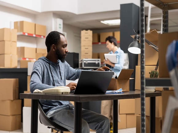 African american warehouse employee running local brand operations, surrounded by shelving units and packages. Person managing logistics and custom order systems in a storage room_2649066423