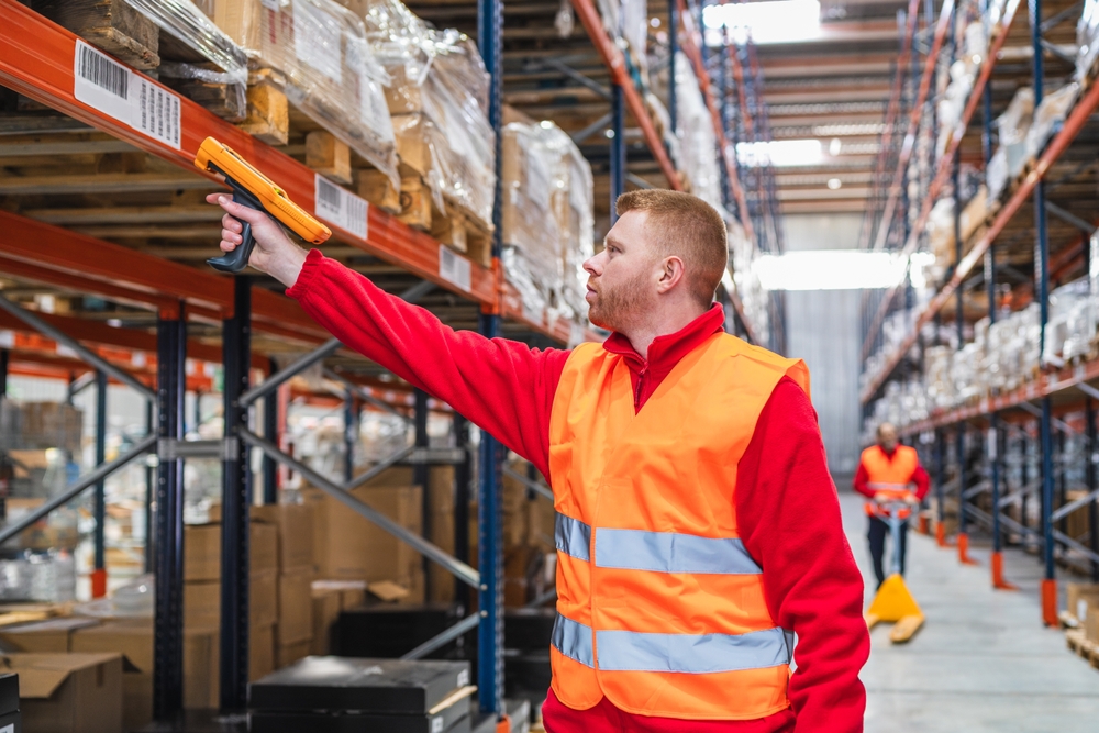 Warehouse worker scanning barcodes on packages using a handheld scanner, managing inventory and logistics in a distribution center