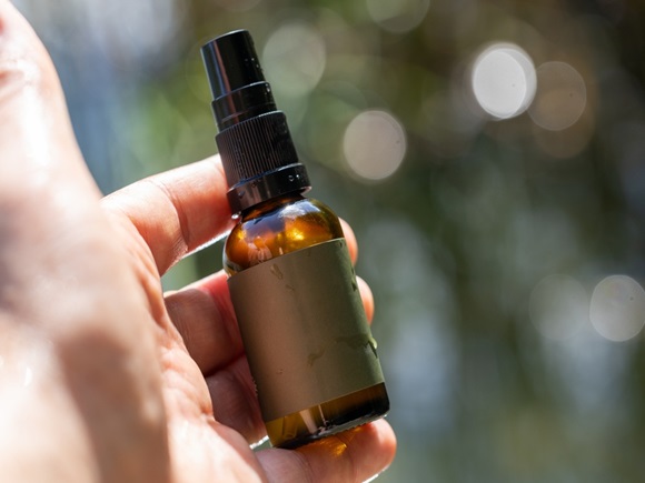 Close-up of a hand holding a small brown glass spray bottle with a blurred natural background_id2502508565