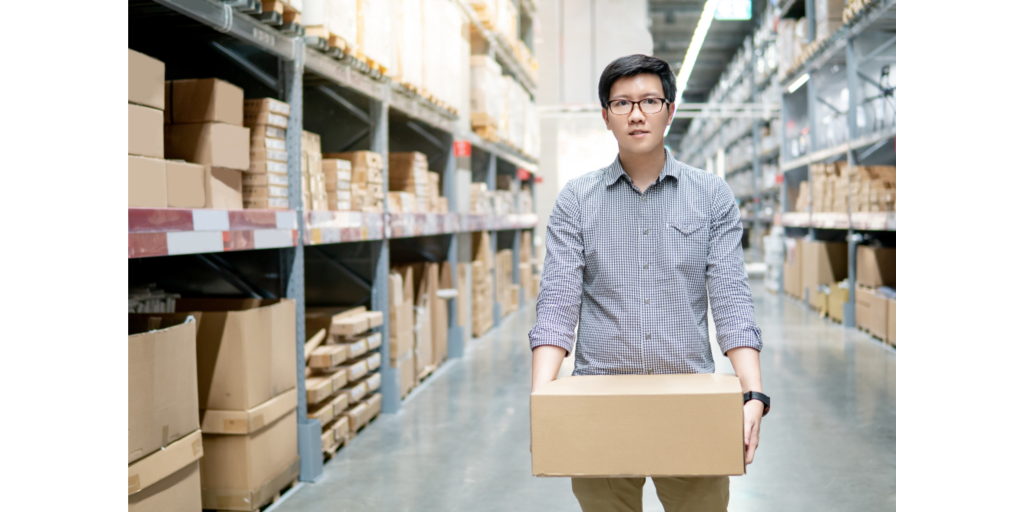 Young Asian man carrying cardboard box between row of shelves in warehouse. Shopping warehousing or working pick and packing concepts_id1284908767