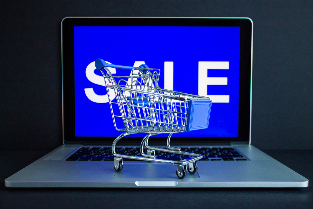 Metal shopping basket on the computer close-up and the inscription on the screen - sale on a blue background. The concept of online shopping_id1722222652