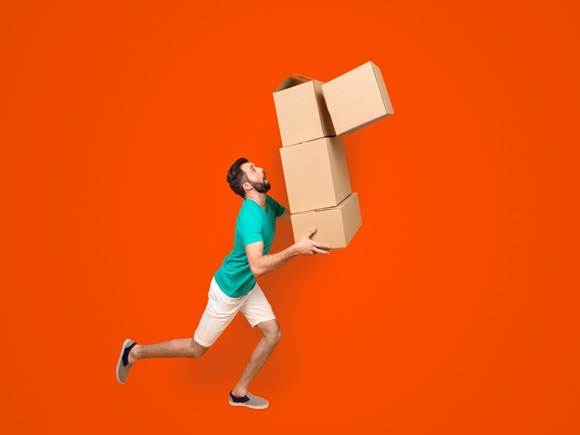 Funny nervous man is carrying his stuff in boxes to the recently bought flat. He is holding cardboard boxes and one is falling down, isolated on yellow background _id2258695035
