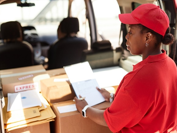 Woman in red shirt and cap organizing packages in vehicle, preparing them for delivery. Image captures her side profile working diligently in organized workspace _id2506823799
