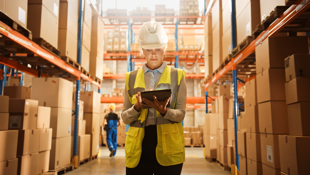 Professional Confident Worker Wearing Hard Hat Checks Stock and Inventory with Digital Tablet Computer in the Retail Warehouse full of Shelves with Goods. Working in Logistics, Distribution Center _id1845773644