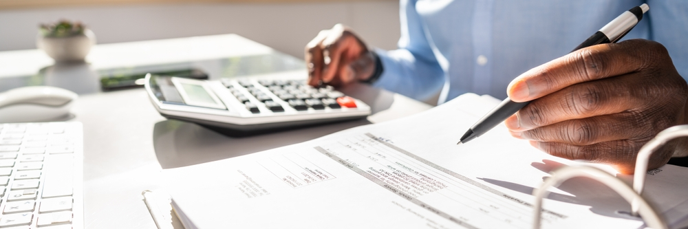 Happy Young Businessman Calculating Invoice On Computer Screen Near Laptop