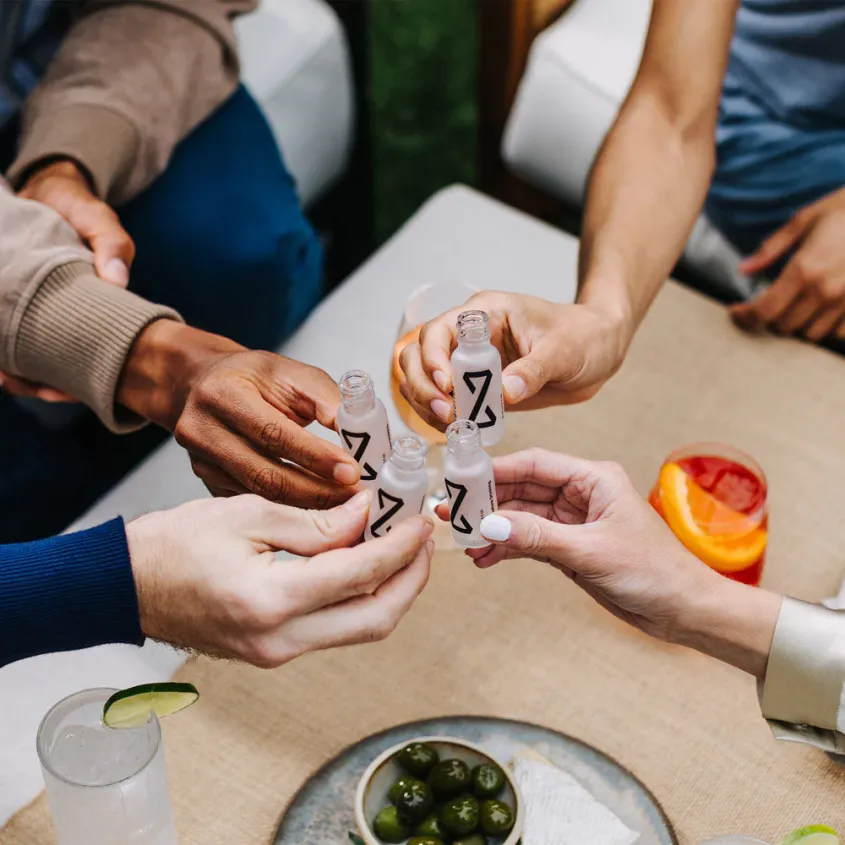 A close-up of people's hands holding Zbiotics' probiotic drinks in the act of a cheers